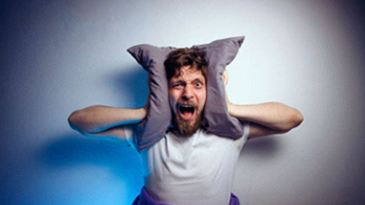 Man holding a pillow over his ears and screaming in frustration 