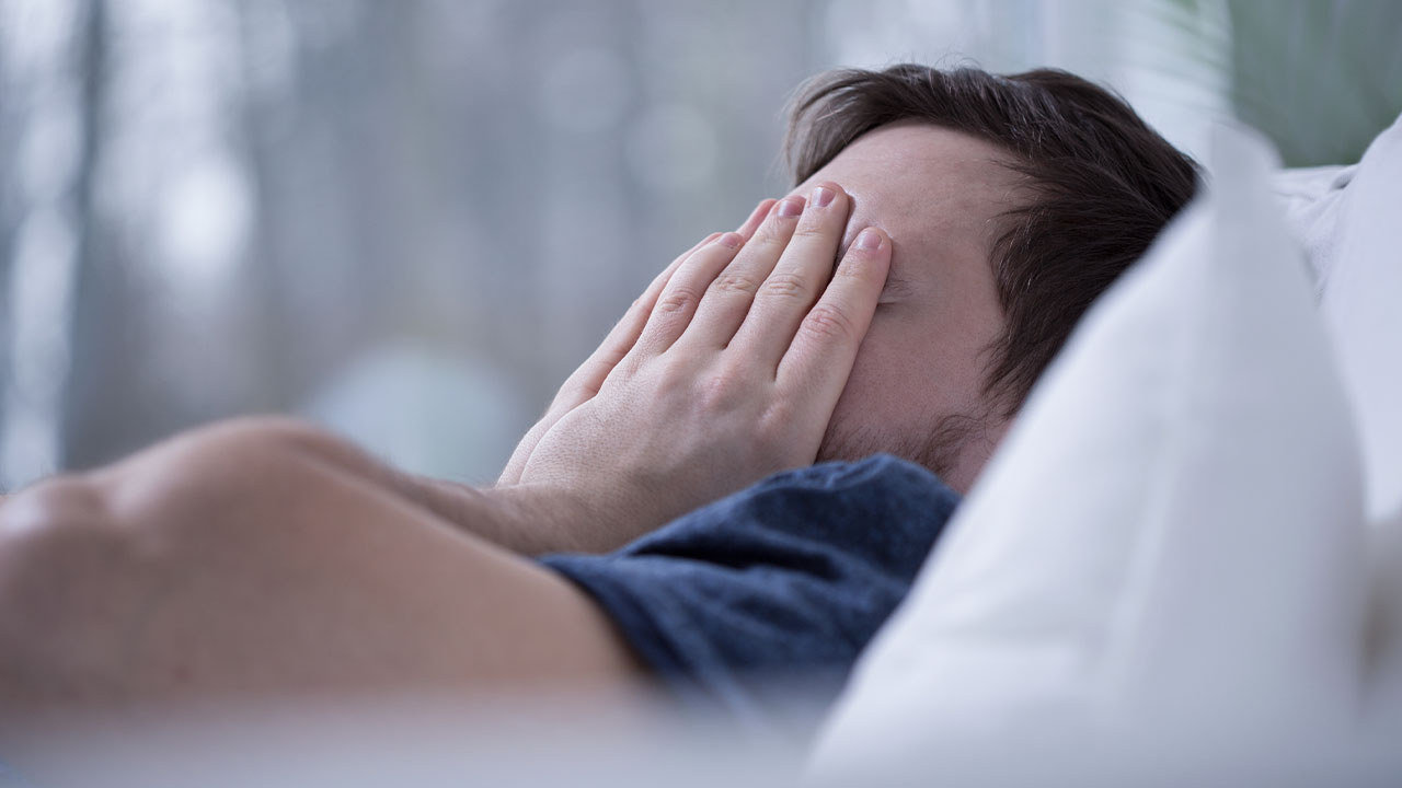 Man lying in bed with white sheets and snoring