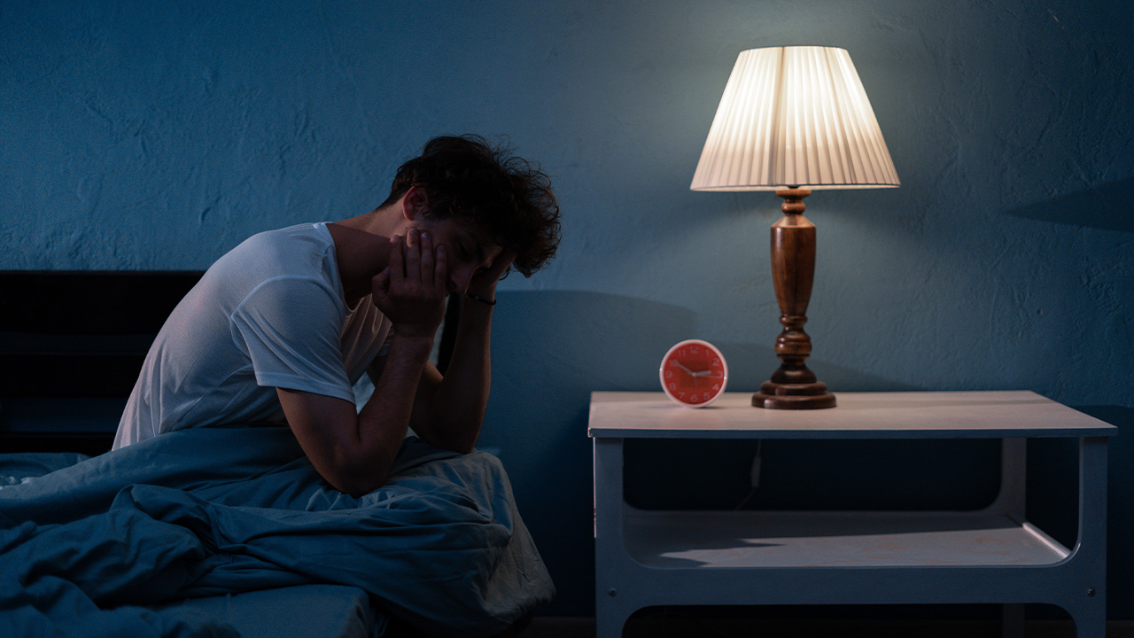 man sitting on edge of bed not able to sleep