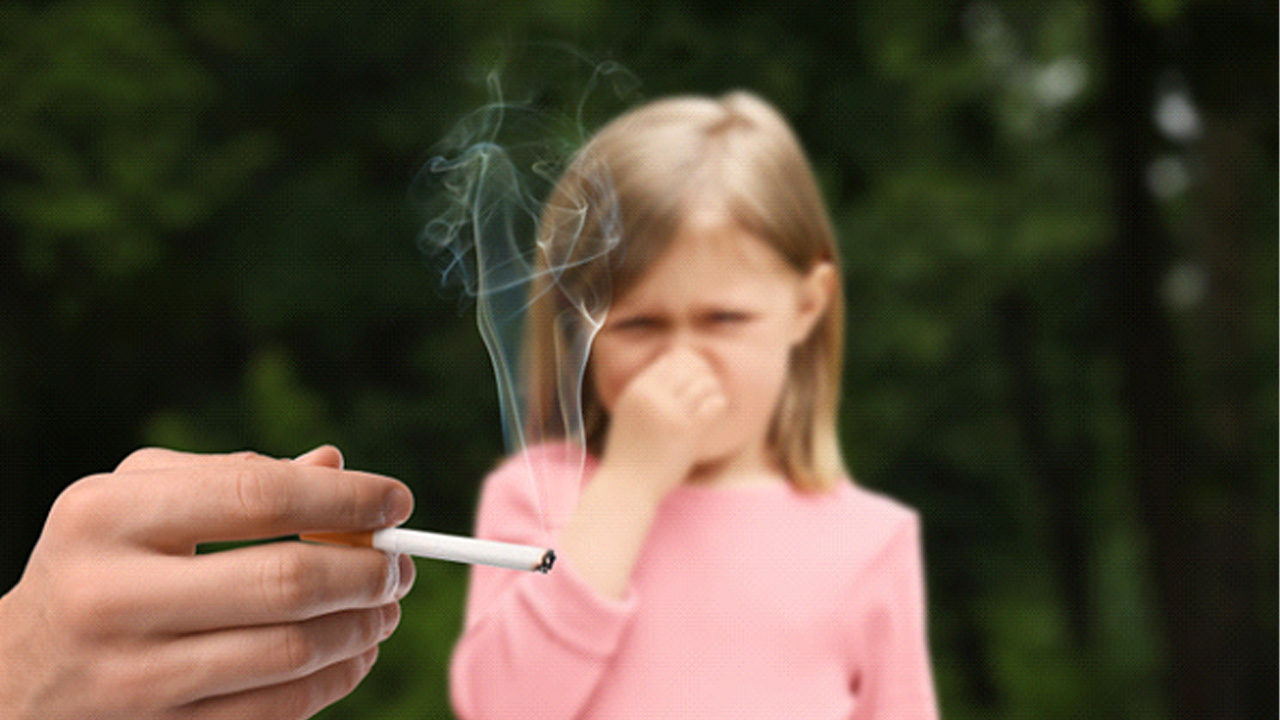 Child covering her mouth while adult smokes nearby